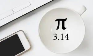 Biały kubek z symbolem π i liczbą 3.14, obok smartfon i fragment laptopa.
