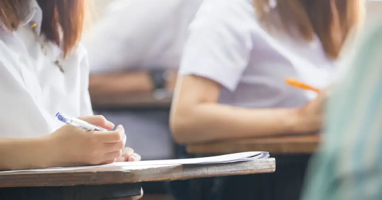 Dłoń studenta pisząca długopisem na kartce papieru podczas egzaminu.